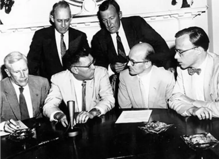 Umgeben-von-US-Wissenschaftlern-verkuendet-der-Sprecher-des-Praesidenten-James-Haggerty-vor-dem-Mikrofon-die-USA-werden-den-ersten-menschgemachten-Satelliten-ins-All-schiessen