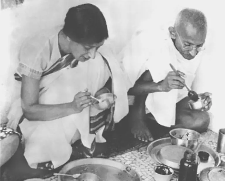 Dem-Tragen-traditioneller-indischer-Kleidung-entspricht-der-einfache-Lebensstil-Gandhis-Er-gruendet-einen-Ashram-eine-klosteraehnliche-Siedlung-in-der-fuer-indische-Verhaeltnisse-nahezu-revolutionaer-auch-Frauen-und-Unberuehrbare-gleichberechtigt-sind