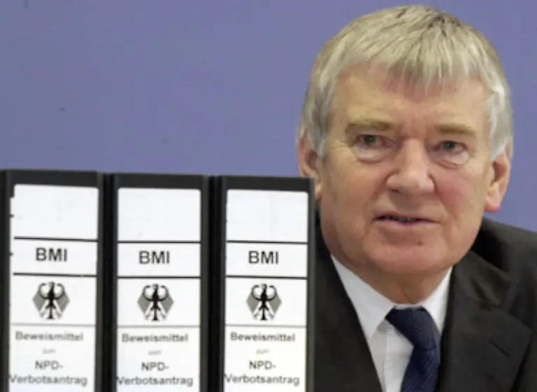 Das-Verfahren-ist-ein-politisch-gewagtes-Manoever-Schily-scheitert-Nach-langem-Hin-und-Her-auf-Grund-der-V-Mann-Affaere-stellt-Karlsruhe-das-NPD-Verbotsverfahren-im-Maerz-2003-endgueltig-ein-Schily-sieht-sich-mit-Ruecktrittsforderungen-konfrontiert-bleibt-jedoch-im-Amt