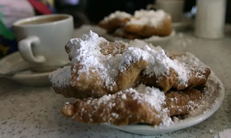 Hier-gibt-es-eine-franzoesische-Spezialitaet-Suesse-noch-dampfende-Beignets-mit-Bergen-von-Puderzucker-bedeckt-und-mit-einer-Tasse-Cafe-Au-Lait-serviert
