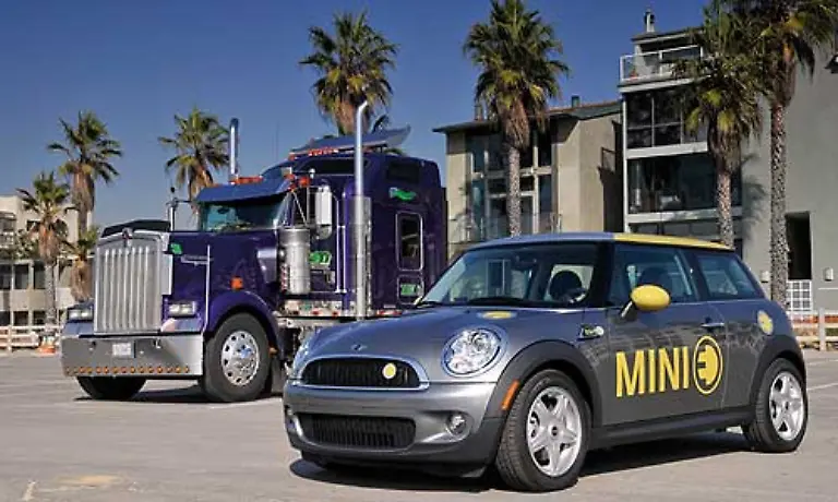 Im-Gegensatz-zu-den-herkoemmlichen-Konzepten-der-Fortbewegung-Im-Hintergrund-ein-Kenworth-Truck-amerikanischer-Bauart-mit-einem-Verbrauch-von-40-bis-60-Litern-erweist-sich-der-Elektro-Mini-als-erstaunlich-alltagstauglich