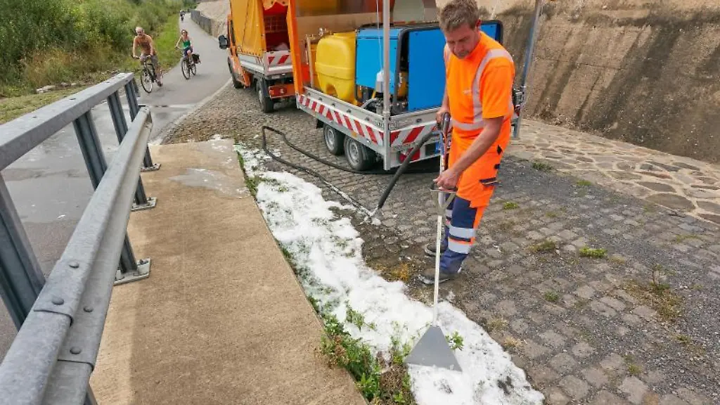 Ein-Strassenwaerter-beseitigt-am-Rand-eines-Radweges-Unkraut-mit-Hilfe-eines-Heissschaumgeraets