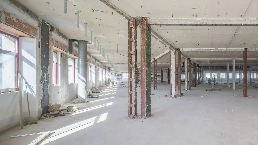 Ein-grosser-leerer-Industrieraum-mit-freiliegenden-Balken-und-verstreuten-Baumaterialien