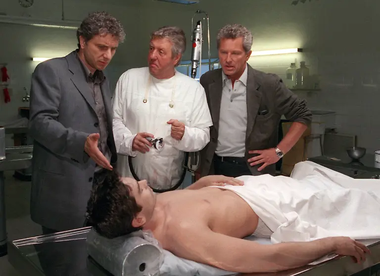 Der-Volksmusikpapst-Karl-Moik-steht-am-9-5-2000-im-Pathologischen-Institut-des-Schwabinger-Krankenhauses-in-Muenchen-in-seiner-Rolle-als-Gerichtsmediziner-fuer-den-neuen-ARD-Tatort-Einmal-taeglich-vor-der-Kamera-neben-ihm-die-Fernsehkommissare-Ivo-Batic-Miroslav-Nemec-r-und-Franz-Leitmayr-Udo-Wachtveitl-l-Mit-der-Nebenrolle-ging-fuer-den-61-jaehrigen-Moik-ein-Traum-in-Erfuellung-den-Gastauftritt-hatte-sich-der-Musikantenstadl-Chef-bereits-zu-seinem-60-Geburtstag-gewuenscht-Moik-obduziert-in-dem-Streifen-die-Leiche-des-jungen-Daily-Soap-Darstellers-und-Frauenschwarms-Peter-Burkhardt-Manou-Lubowski-Bei-den-Dreharbeiten-zu-der-Produktion-des-Bayerischen-Rundfunks-zeigte-sich-Moik-selbstbewusst-und-scherzte-Jetzt-zeig-ich-denen-vom-Film-mal-wie-das-geht-Der-Krimi-wird-am-29-10-ausgestrahlt