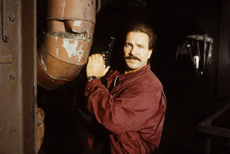 Goetz-George-in-Tatort-Der-Pott-10-88-ru-Mann-Fernsehen-Film-Schauspiel-quer-halb-stehend-Jacke-rot-PISTOLE-dunkelhaarig-Schnaeuzer-ernst