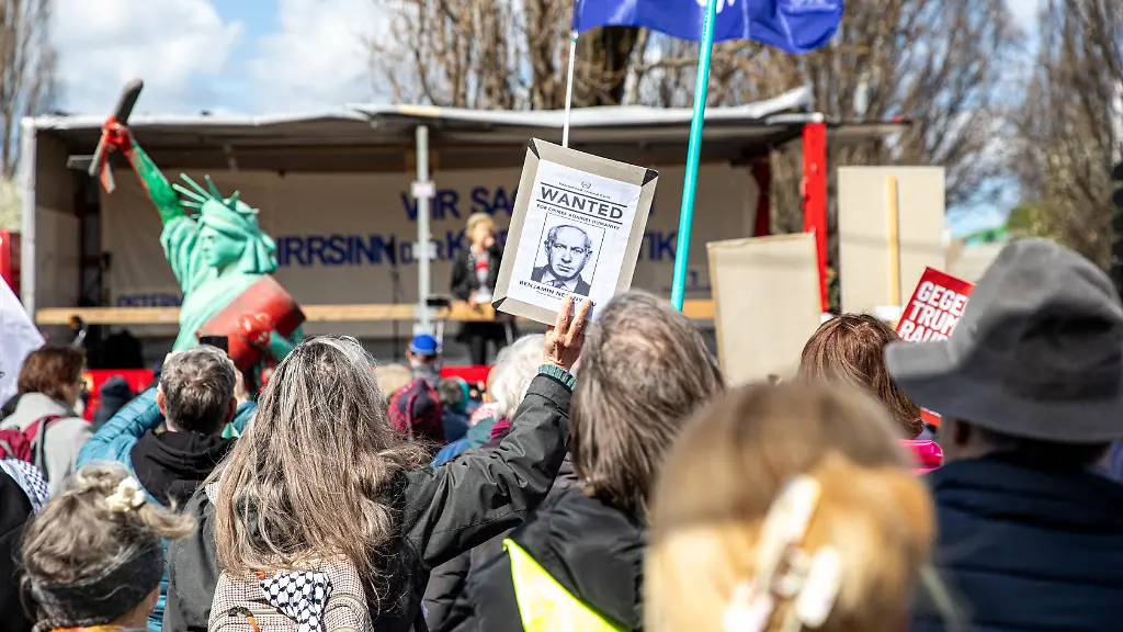 On-Saturday-April-4-2026-demonstrators-gathered-at-Mauerpark-in-Berlin-for-an-Easter-peace-march-where-speakers-and-participants-called-for-an-end-to-military-escalation-and-international-conflicts-Protesters-held-signs-opposing-U-S-President-Donald-Trump-German-Chancellor-Friedrich-Merz-and-Israeli-Prime-Minister-Benjamin-Netanyahu-while-calling-for-peace-and-an-end-to-what-they-described-as-war-and-aggression-During-speeches-participants-urged-the-closure-of-U-S-military-bases-in-Germany-including-Ramstein-Air-Base-and-criticized-NATO-policies-and-increased-defense-spending-Demonstrators-carried-a-range-of-banners-and-flags-including-Palestinian-flags-Iranian-flags-and-peace-flags-featuring-dove-symbols-Some-signs-called-for-an-end-to-what-protesters-described-as-war-drivers-while-others-expressed-opposition-to-U-S-and-Israeli-military-actions-and-showed-solidarity-with-Russia-A-Statue-of-Liberty-prop-covered-in-red-paint-and-holding-an-oil-barrel-is-seen-among-the-crowd-Additional-banners-criticized-NATO-and-called-for-diplomatic-solutions-instead-of-continued-military-support-in-ongoing-conflicts