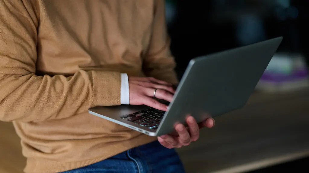 Konzentrierter-maennlicher-Profi-mit-einem-Laptop-waehrend-er-in-einem-modernen-offenen-Bueroraum-steht-mit-Mitarbeitern-die-im-Hintergrund-zusammenarbeiten-die-Produktivitaet-Fokus-und-Teamarbeit-symbolisieren-Modellfreigabe-vorhanden