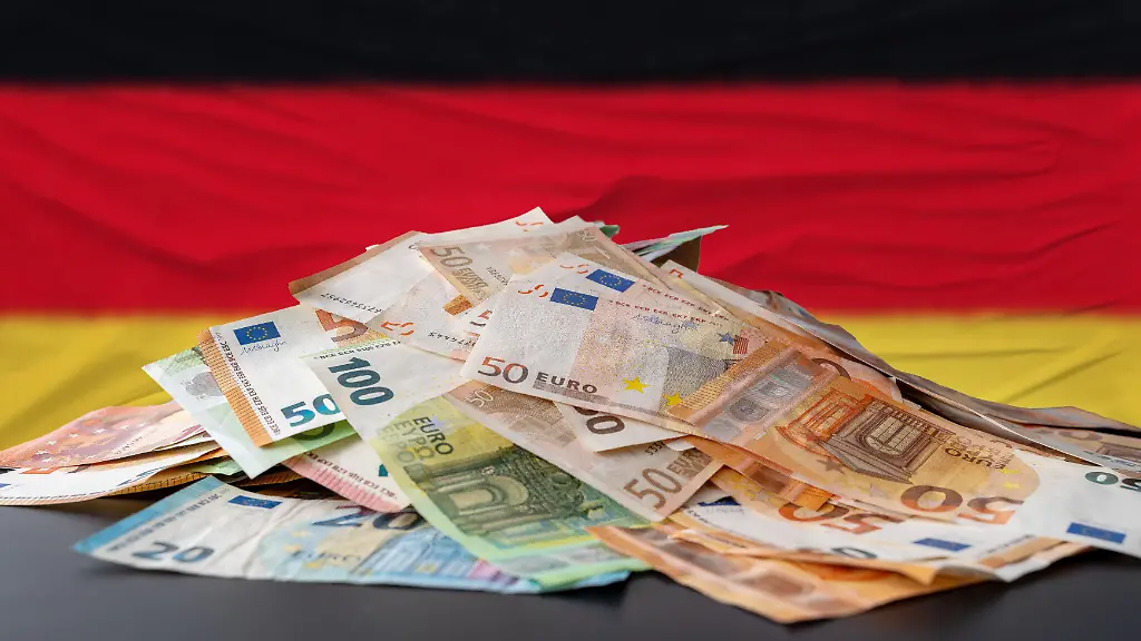 Fotomontage-Konzept-zu-Staatsverschuldung-in-Deutschland-Ein-Haufen-Euro-Banknoten-vor-einer-Deutschlandflagge-symbolisiert-den-wachsenden-Schuldenberg-finanzielle-Belastungen-und-die-angespannte-Haushaltslage-der-Bundesrepublik