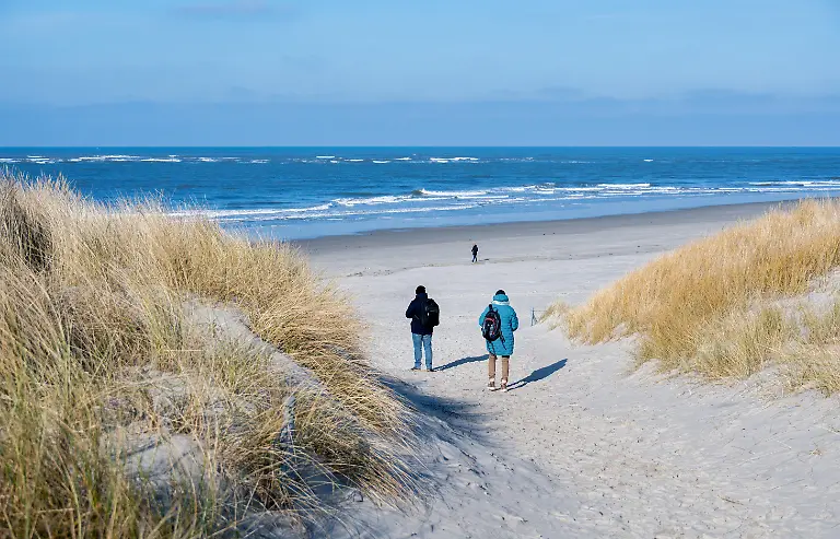 Touristen-gehen-bei-sonnigem-Wetter-ueber-einen-Weg-durch-die-Duenen-am-Strand-der-Nordseeinsel-Langeoog