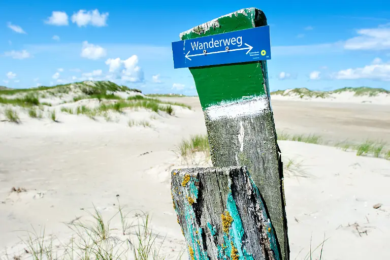 Ein-Holzpfahl-mit-der-Aufschrift-Wanderweg-steht-in-der-Duenenlandschaft-am-Ostende-der-Insel