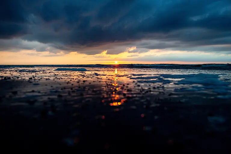 Die-Sonne-geht-am-Strandabschnitt-Weisse-Duene-ueber-der-Nordsee-unter-und-spiegelt-sich-dabei-in-den-Wellen