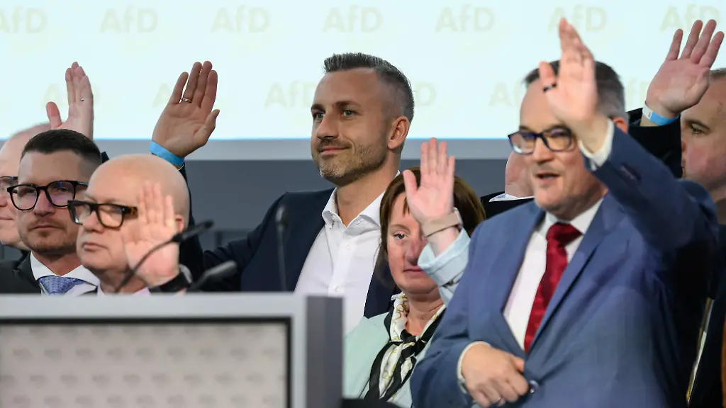 Martin-Reichardt-vorn-Landesvorsitzender-der-AfD-Sachsen-Anhalt-und-Ulrich-Siegmund-3-v-r-Spitzenkandidat-fuer-die-Landtagswahl-2026-heben-ihre-Haende-waehrend-der-Abstimmung-ueber-das-Regierungsprogramm-auf-dem-Landesparteitag-der-AfD-Sachsen-Anhalt-in-Magdeburg-Die-Delegierten-des-Landesparteitages-wollen-das-Regierungsprogramm-zur-Landtagswahl-2026-final-erarbeiten-und-beschliessen
