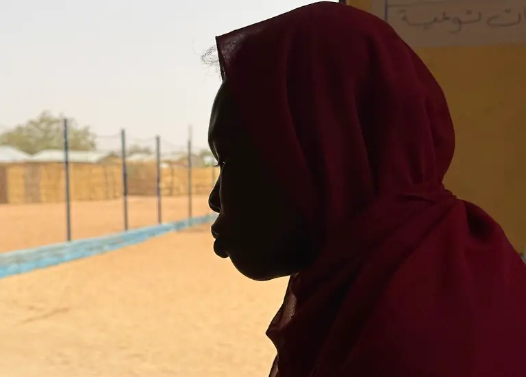 Eine-sudanesische-Frau-steht-im-Fluechtlingslager-Aboutenge-im-Osten-des-Tschad-Im-Buergerkrieg-im-Sudan-setzt-die-Miliz-Rapid-Support-Forces-RSF-systematisch-sexuelle-Gewalt-als-Kriegswaffe-gegen-nicht-arabische-Bevoelkerungsgruppen-ein-Die-Scham-und-das-Stigma-sind-gross-Vielen-betroffenen-Frauen-und-Maedchen-faellt-es-schwer-ueber-das-Erlebte-zu-sprechen