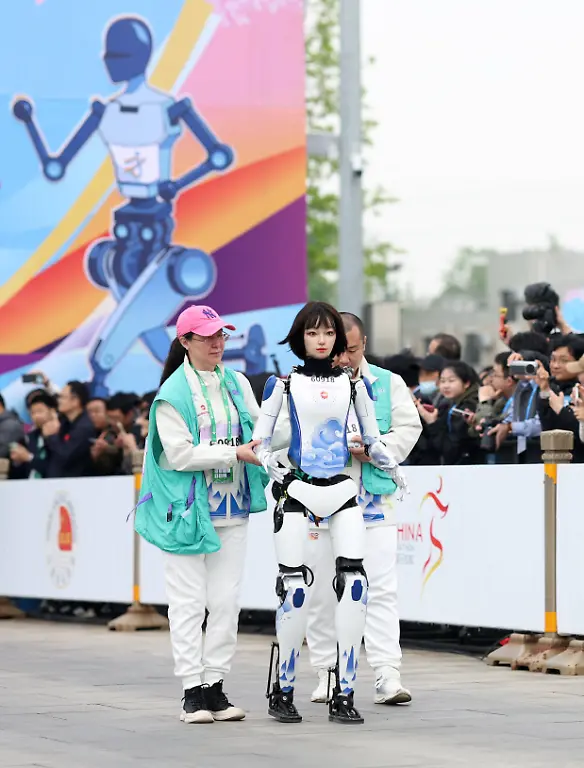China-Roboter-nehmen-am-Peking-E-Town-Halbmarathon-teil-250419-BEIJING-April-19-2025-Robotic-participant-Huanhuan-front-competes-as-engineers-run-alongside-during-the-Beijing-E-Town-half-marathon-and-humanoid-robots-half-marathon-in-the-Beijing-Economic-Technological-Development-Area-in-southeast-Beijing-April-19-2025