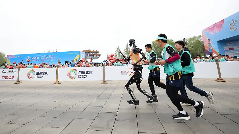 China-Roboter-nehmen-am-Peking-E-Town-Halbmarathon-teil-250419-BEIJING-April-19-2025-Robotic-participant-Tiangong-Ultra-front-L-competes-as-engineers-runs-alongside-during-the-Beijing-E-Town-half-marathon-and-humanoid-robots-half-marathon-in-the-Beijing-Economic-Technological-Development-Area-in-southeast-Beijing-April-19-2025