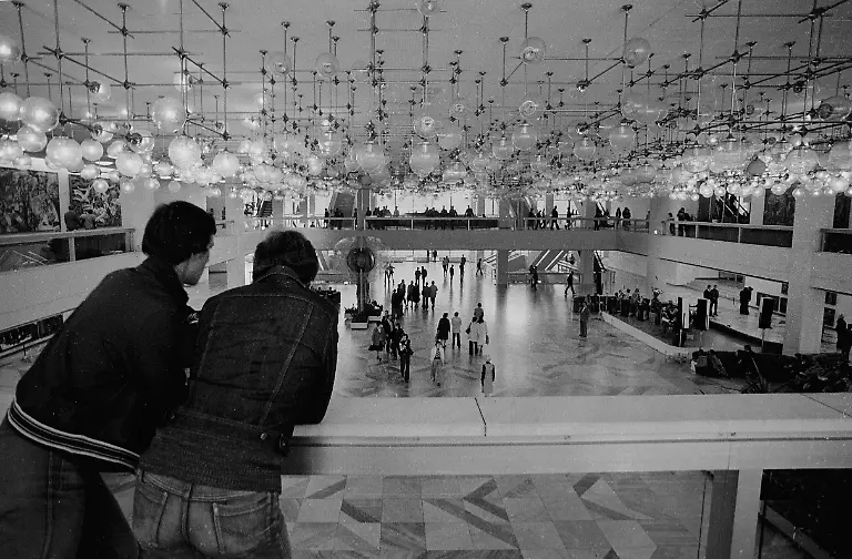 Zwei-Besucher-schauen-in-die-Eingangshalle-des-Palastes-der-Republik-PdR-am-Marx-Engels-Platz-heute-Schlossplatz-Wegen-seiner-Beleuchtung-wurde-der-Palast-der-Republik-von-den-Ost-Berlinern-auch-Erichs-Lampenladen-genannt-Mittig-im-Bild-ist-das-im-Foyer-ausgestellte-fuenf-Meter-hohe-Kunstwerk-Glaeserne-Blume-zu-sehen-Anstelle-des-1950-abgerissenen-Stadtschlosses-wurde-ab-1973-der-Palast-der-Republik-gebaut-180m-lang-und-32m-breit-Verschiedenen-Einrichtungen-waren-dort-untergebracht-so-z-B-die-DDR-Volkskammer-im-kleinen-Saal-Im-grossen-Saal-fanden-Veranstaltungen-statt-er-fasste-5000-Besucher-Des-Weiteren-gab-es-Restaurants-und-Cafes-fuer-1500-Gaeste-Die-Planung-des-Bauwerks-unterlag-einem-Architektenkollektiv-unter-der-Leitung-von-Heinz-Graffunder-Undatierte-Aufnahme-Anfang-der-1990er-Jahre-in-Berlin-Foto-Paul-Glaser-GESPERRT-FUeR-BILDFUNK-Local-Caption-East-Berlin-The-entrance-of-the-Palace-of-the-Republic-Palast-der-Republik-PdR-and-the-five-meter-tall-artwork-Glassy-flower-Glaeserne-Blume-Because-of-its-lightning-it-was-also-called-Erich-s-lamp-shop-Erichs-Lampenladen-from-the-citizen-of-East-Berlin-Instead-of-the-Berlin-City-Palace-Berliner-Stadtschloss-which-was-teared-down-in-1950-the-Palace-of-the-Republic-was-build-180m-long-and-32m-broad-The-People-s-Chamber-of-the-GDR-DDR-Volkskammer-had-its-meetings-there-A-collective-of-architects-made-the-construction-schedules-under-the-guidance-of-Heinz-Graffunder