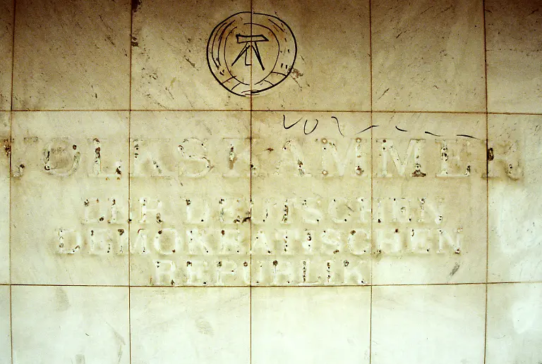 Ein-verblasster-Schriftzug-Volkskammer-Deutsche-Demokratische-Republik-und-ein-aufgemaltes-Emblem-der-DDR-nach-der-Demontage-der-Buchstaben-am-Palast-der-Republik-dem-einstigen-Sitz-der-DDR-Volkskammer-aufgenommen-im-September-1990