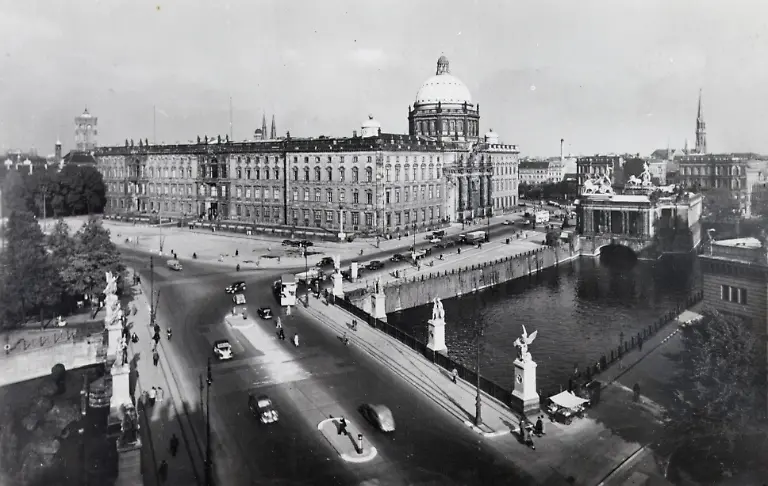 15-09-1938-Berlin-Von-Unter-den-Linden-kommend-die-Schlossbruecke-ueberquerend-betritt-man-den-Schlossplatz-Hier-stand-das-Berliner-Stadtschloss-das-auf-eine-unter-Kurfuerst-Friedrich-II-1443-bis-1451-errichtete-Burg-zurueckging-Das-gewaltige-Schlossgebaeude-erstreckte-sich-mit-200-Meter-Laenge-120-Meter-Breite-und-einer-70-Meter-hohen-Kuppel-ueber-das-gesamte-Areal-Seine-allseits-gepriesene-barocke-Form-und-die-praechtige-Innenausstattung-verdankte-es-dem-um-1700-vorgenommenen-Ausbau-durch-Andreas-Schlueter-der-hier-sein-Meisterwerk-schuf-Nach-1945-war-das-Schloss-eine-ausgebrannte-Ruine-fuer-deren-Wiederaufbau-sich-jedoch-viele-Experten-und-auch-viele-Berliner-aussprachen-Doch-die-damalige-DDR-Fuehrung-hatte-andere-Plaene-Sie-sah-im-Schloss-ein-Symbol-fuer-die-feudalistische-und-imperialistische-Vergangenheit-Deutschlands-mit-der-es-nun-vorbei-sei-und-ordnete-die-Sprengung-der-Ruine-an-die-1950-erfolgte-Es-entstand-ein-weiter-leerer-Platz-fuer-Demonstrationen-und-Aufmaersche-der-schliesslich-mit-dem-Palast-der-Republik-bebaut-wurde