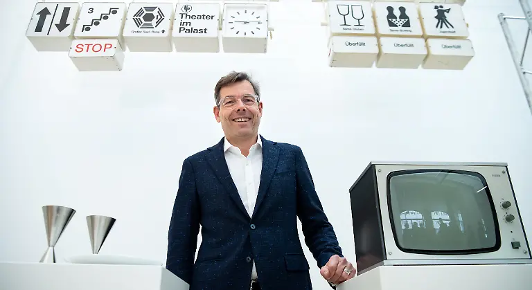 Hartmut-Dorgerloh-Generalintendant-des-Humboldt-Forums-steht-anlaesslich-einer-Pressekonferenz-zur-Praesentation-des-Palastes-der-Republik-im-Humboldt-Forum-zwischen-Eiskaffeebechern-und-einem-Ueberwachungsmonitor-aus-dem-Palast-der-Republik-im-Hintergrund-haengen-Teile-des-ehemaligen-Wegeleitsystems-Die-Stiftung-Humboldt-Forum-im-Berliner-Schloss-wird-im-Humboldt-Forum-auch-die-facettenreiche-Geschichte-des-Ortes-praesentieren-Der-Palast-der-Republik-wird-dabei-eine-wichtige-Rolle-spielen