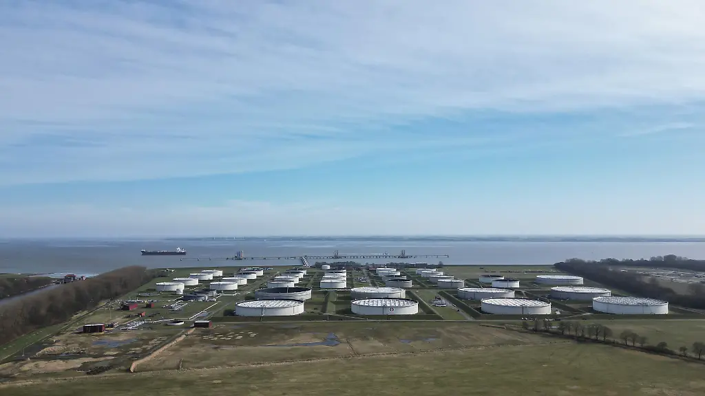 Ein-Oeltanker-liegt-an-der-Tankerloeschbruecke-der-Nord-West-Oelleitung-NWO-auf-der-Jade-bei-Wilhelmshaven-im-Vordergrund-stehen-grosse-Lagertanks-eines-Mineraloeltanklagers-Luftaufnahme-mit-einer-Drohne-Ueber-Hafenanlagen-Pipelines-und-Tanklager-werden-Rohoel-und-Mineraloelprodukte-angeliefert-gespeichert-und-weitertransportiert-die-Infrastruktur-ist-Teil-der-Energieversorgung-in-Deutschland