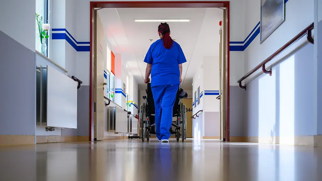 Eine-Pflegerin-der-Geriatrie-im-DRK-Krankenhaus-Chemnitz-schiebt-einen-Patienten-im-Rollstuhl-ueber-die-Station-Die-Geriatrie-ist-auf-die-medizinische-Versorgung-aelterer-Patienten-spezialisiert