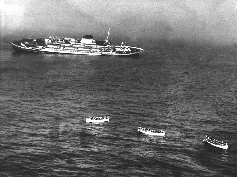 Das-italienische-Luxusschiff-Andrea-Doria-sinkt-am-26-07-1956-nach-einem-Zusammenstoss-mit-dem-schwedischen-Dampfer-Stockholm-vor-der-amerikanischen-Ostkueste-Im-Vordergrund-sind-drei-Rettungsboote-zu-sehen-Ueber-1650-Passagiere-konnten-gerettet-werden-51-Menschen-kamen-ums-Leben-Aufnahme-vom-26-07-1956-Achtung-Die-Angaben-zur-Zahl-der-Toten-bei-dem-Zusammenstoss-der-Andrea-Doria-und-der-Stockholm-schwanken-In-einigen-Quellen-wird-von-insgesamt-46-Toten-berichtet-andere-sprechen-von-46-Toten-auf-der-Andrea-Doria-und-fuenf-auf-der-Stockholm