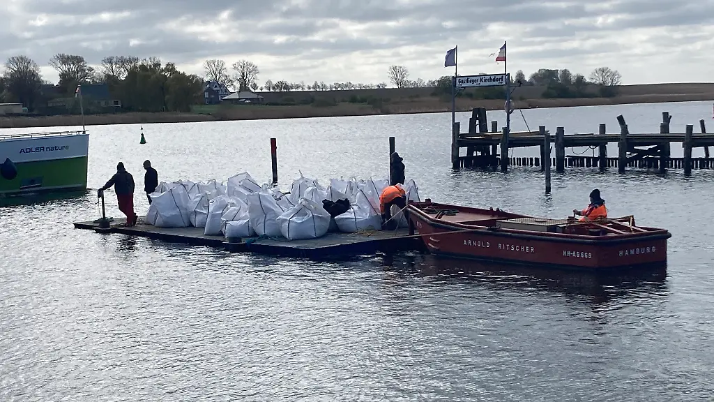Grosse-Sandsaecke-sogenannte-Big-Bags-liegen-im-Hafen-von-Kirchdorf-auf-Poel-auf-einem-Ponton-der-von-einem-Boot-geschoben-wird-Der-gestrandete-Buckelwal-liegt-weiterhin-im-Flachwasser-fest-Eine-private-Initiative-versucht-seit-Tagen-den-Wal-zu-retten