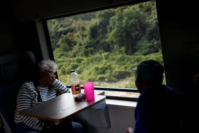 Tourists-look-out-the-window-while-traveling-from-Bacalar-to-Chetumal-aboard-a-carriage-of-the-Maya-Train-in-Bacalar-Quintana-Roo-state-Mexico-November-12-2025-The-Mayan-Train-has-struggled-to-attract-the-expected-interest-after-legal-challenges-environmental-rerouting-and-land-constraints-pushed-key-segments-inland-leaving-many-stations-far-from-city-centers-and-airports-Reuters-visits-in-November-2025-found-mostly-empty-stations-and-lightly-occupied-trains-as-projected-annual-ridership-was-cut-to-1-2-million-and-the-project-s-cost-swelled-to-more-than-25-billion-with-revenues-covering-less-than-13-of-operating-costs-REUTERS-Daniel-Becerril-SEARCH-BECERRIL-MAYA-TRAIN-FOR-THIS-STORY-SEARCH-WIDER-IMAGE-FOR-ALL-STORIES