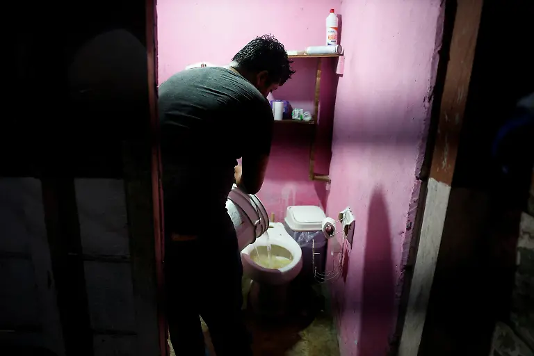 Carlos-Augusto-Gonzalez-pours-a-bucket-of-collected-rainwater-to-flush-a-toilet-because-of-a-lack-of-drinking-water-supply-in-Xpujil-Campeche-state-Mexico-November-13-2025-Mexico-s-1-500-km-Mayan-Train-was-launched-to-drive-development-in-the-country-s-impoverished-south-through-infrastructure-and-tourism-but-two-years-after-its-inauguration-it-is-struggling-financially-ticket-sales-cover-only-a-fraction-of-costs-hotels-remain-largely-empty-and-communities-along-the-route-say-poverty-persists-and-promised-benefits-have-yet-to-materialize-A-Reuters-review-of-census-data-and-interviews-with-residents-along-the-line-found-that-poverty-remains-widespread-and-well-paid-jobs-scarce-despite-the-project-REUTERS-Daniel-Becerril-SEARCH-BECERRIL-MAYA-TRAIN-FOR-THIS-STORY-SEARCH-WIDER-IMAGE-FOR-ALL-STORIES