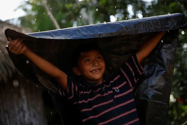 Leyner-Jesus-Chan-Kumul-a-member-of-a-Mayan-family-shields-himself-from-the-rain-with-a-plastic-bag-while-playing-in-the-yard-of-his-grandparents-home-in-Uh-May-Quintana-Roo-state-Mexico-November-16-2025-Historically-marginalized-Maya-populations-in-Mexico-s-southeast-have-long-faced-high-poverty-rates-and-limited-access-to-services-and-while-the-Mayan-Train-was-promoted-as-a-way-to-bring-development-to-Indigenous-Maya-communities-many-community-activists-say-instead-that-their-forests-have-been-fragmented-communal-lands-eroded-and-traditions-strained-For-many-Maya-the-land-over-which-it-runs-is-their-sacred-inheritance-central-to-their-identity-and-linking-them-to-their-ancestors-REUTERS-Daniel-Becerril-SEARCH-BECERRIL-MAYA-TRAIN-FOR-THIS-STORY-SEARCH-WIDER-IMAGE-FOR-ALL-STORIES