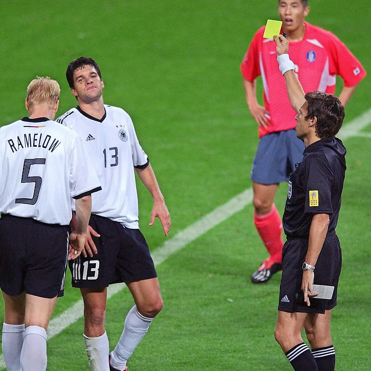 Der-Schweizer-Schiedsrichter-Urs-Meier-r-vorn-zeigt-dem-deutschen-Mittelfeldspieler-Michael-Ballack-2-v-l-die-Gelbe-Karte-An-Ballacks-Seite-Carsten-Ramelow-l-Die-deutsche-Fussballnationalmannschaft-gewinnt-am-25-06-2002-in-Seoul-das-Halbfinalspiel-des-17-WM-Turniers-gegen-die-Elf-des-Gastgebers-Suedkorea-durch-Ballacks-Tor-mit-1-0-und-qualifiziert-sich-damit-zum-siebentenmal-fuer-das-Endspiel-in-dem-Ballack-nach-seiner-zweiten-Gelben-Karte-fehlt