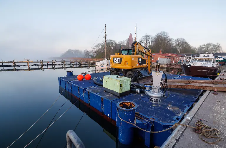 Ein-Bagger-steht-am-Morgen-auf-einem-Ponton-und-soll-spaeter-bei-der-Rettung-des-Buckelwals-vor-der-Ostseeinsel-Poel-eingesetzt-werden-Fuer-den-vor-der-Insel-Poel-gestrandeten-Buckelwal-hat-ein-neuer-Rettungsversuch-begonnen-Umgesetzt-wird-das-Konzept-von-einer-privaten-Initiative