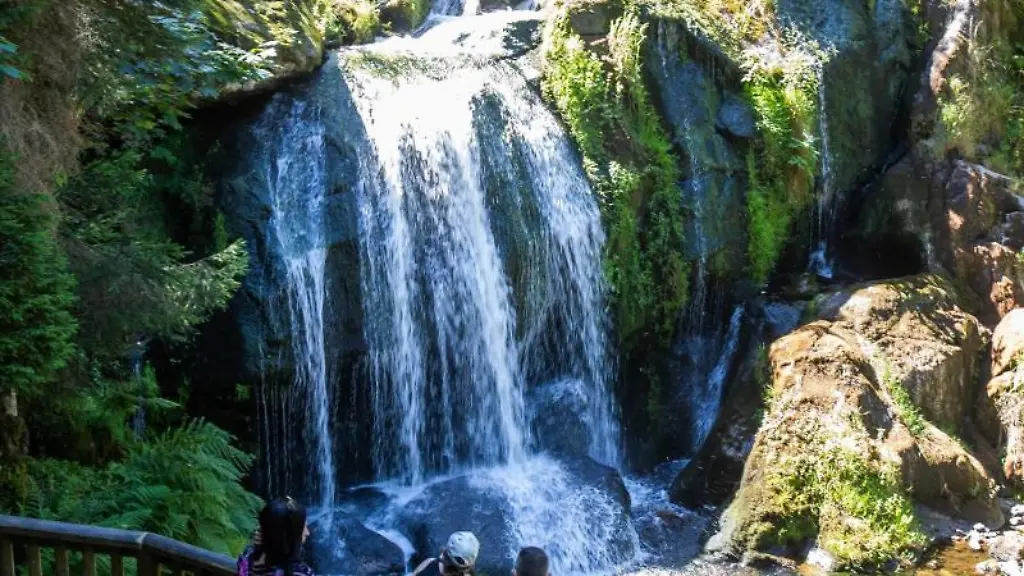 Touristen-stehen-auf-einer-Aussichtsplattform-und-blicken-auf-eine-Stufe-der-Triberger-Wasserfaelle-ueber-die-Wasser-fliesst
