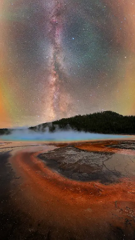 Framed-by-the-vibrant-colors-and-drifting-steam-of-Grand-Prismatic-Spring-the-Milky-Way-rises-above-one-of-the-most-unique-geothermal-landscapes-on-Earth-It-is-a-rare-moment-where-the-raw-energy-of-the-planet-meets-the-quiet-vastness-of-the-night-sky-The-constantly-shifting-steam-transformed-the-scene-from-one-moment-to-the-next-briefly-revealing-the-stars-before-concealing-them-again-By-carefully-timing-the-intervals-between-changes-in-the-wind-the-Milky-Way-became-visible-accompanied-by-a-pronounced-display-of-airglow-that-added-depth-and-atmosphere-to-the-sky