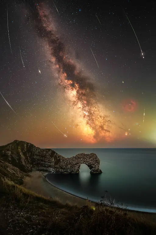 Ancient-fireworks-from-Comet-Swift-Tuttle-hurtled-through-the-atmosphere-to-document-this-ultra-wide-angle-composite-image-above-the-natural-limestone-arch-of-Durdle-Door-In-the-foreground-a-singular-glow-worm-was-documented-amongst-reeds-along-the-sea-cliff-edge-As-the-subject-of-Astrophotography-grows-by-demand-beauty-hotspots-and-World-Heritage-Sites-including-Durdle-Door-are-getting-busy-With-good-reason-that-is-why-as-Astrophotographers-we-need-to-set-an-example-in-protecting-beauty-hotspots-and-local-ecology-Through-practice-of-utilising-red-head-torches-and-adhering-to-access-restricted-areas-of-UNESCO-World-Heritage-sites