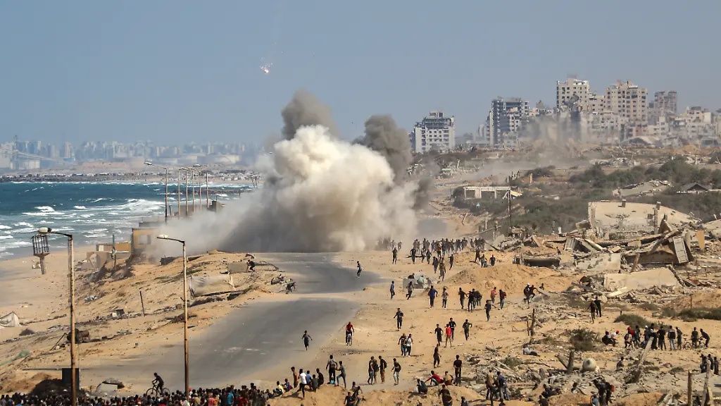 Palaestinenser-machen-sich-von-Nuseirat-im-zentralen-Gazastreifen-aus-auf-den-Weg-entlang-der-Al-Rashid-Strasse-in-Richtung-Gaza-waehrend-eine-Explosion-zu-hoeren-ist-die-mutmasslich-von-Raketenbeschuss-herruehrt-nachdem-sich-Israel-und-die-Hamas-auf-eine-Pause-in-ihrem-Krieg-und-die-Freilassung-der-restlichen-Geiseln-geeinigt-haben