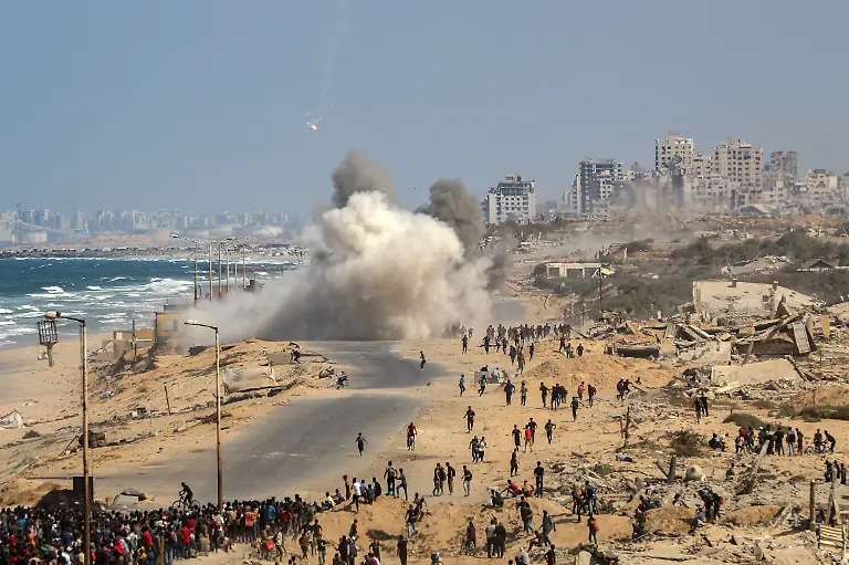 Palaestinenser-machen-sich-von-Nuseirat-im-zentralen-Gazastreifen-aus-auf-den-Weg-entlang-der-Al-Rashid-Strasse-in-Richtung-Gaza-waehrend-eine-Explosion-zu-hoeren-ist-die-mutmasslich-von-Raketenbeschuss-herruehrt-nachdem-sich-Israel-und-die-Hamas-auf-eine-Pause-in-ihrem-Krieg-und-die-Freilassung-der-restlichen-Geiseln-geeinigt-haben