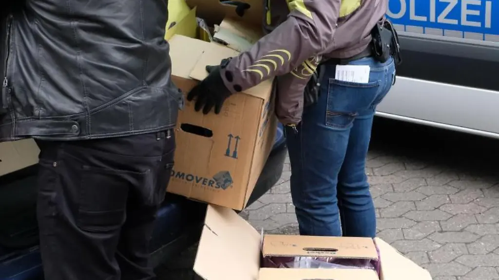 Zwei-Polizeibeamte-in-Zivil-stellen-Kartons-mit-beschlagnahmten-Unterlagen-in-einen-PKW