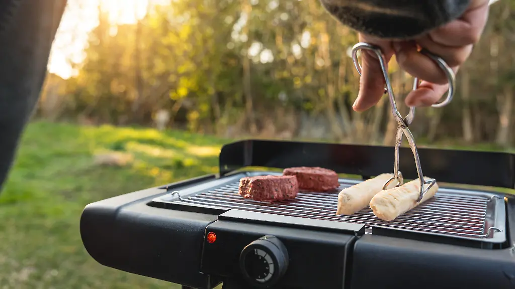 Junger-Mann-grillt-im-Garten-bei-schoenem-Wetter-auf-einem-Elektrogrill