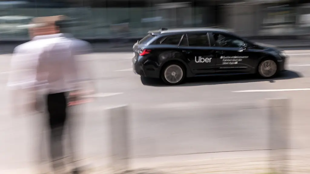14-08-25-Frankfurt-Symbolfoto-Illustrationsbild-Symbolbild-Illustrationsfoto-Alltagsszene-Ein-schwarzes-Fahrzeug-mit-Uber-Branding-faehrt-durch-das-Bankenviertel-in-Frankfurt-am-Main-Im-Vordergrund-steht-unscharf-ein-Passant-dessen-Bewegung-im-Kontrast-zur-Dynamik-des-Fahrzeugs-steht-Das-Bild-ist-mit-Mitziehtechnik-aufgenommen-und-thematisiert-die-Geschwindigkeit-und-Gleichzeitigkeit-urbaner-Mobilitaetsformen-im-digitalen-Zeitalter