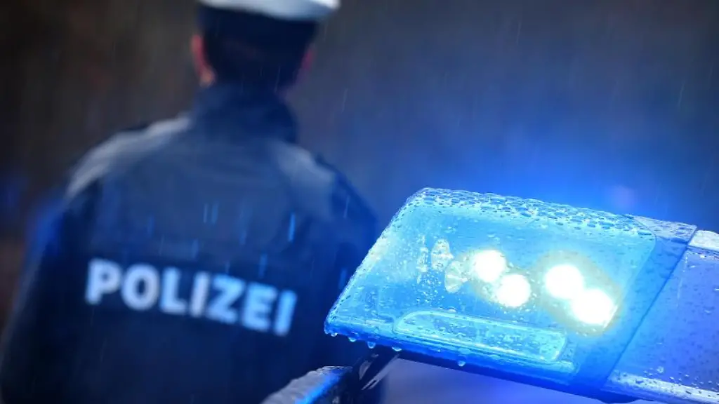 Ein-Polizist-steht-vor-einem-Streifenwagen-dessen-Blaulicht-aktiviert-ist