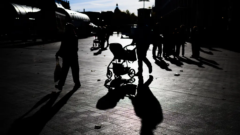 Ein-Mann-schiebt-im-Gegenlicht-der-Sonne-einen-Kinderwagen-durch-die-Innenstadt-und-wirft-dabei-einen-langen-Schatten-auf-den-Boden