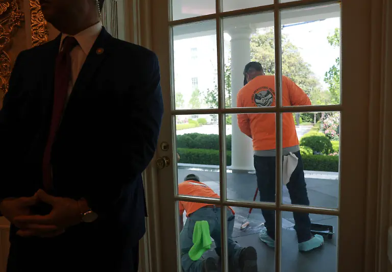 Workers-buff-the-new-black-granite-tiles-on-the-colonnade-as-a-U-S-Secret-Service-agent-stands-near-the-door-of-the-Oval-Office-during-remarks-to-reporters-by-President-Donald-Trump-at-the-White-House-in-Washington-D-C-U-S-April-30-2026