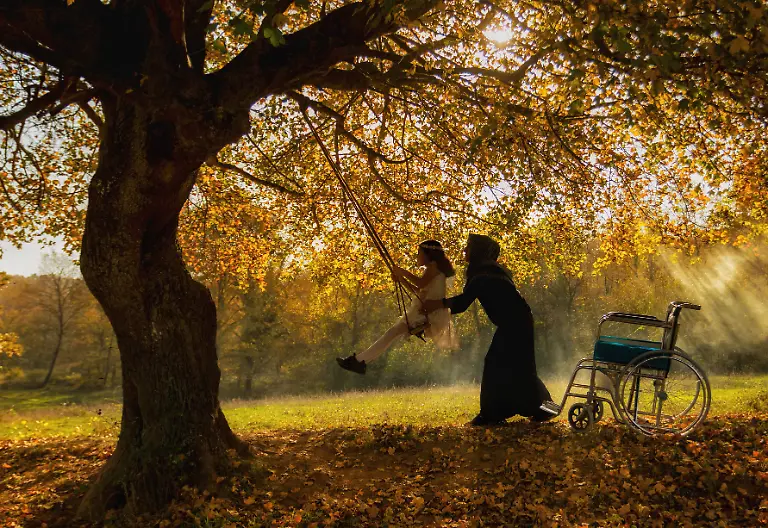 It-s-a-beautiful-sunny-day-the-leaves-of-the-trees-bright-with-autumn-colors-Her-mother-is-probably-trying-to-make-her-disabled-daughter-happy-by-taking-her-on-a-swing-set-up-in-the-lap-of-nature-It-s-essential-for-individuals-with-disabilities-to-be-taken-out-of-city-life-and-taken-out-into-the-countryside-to-increase-their-joy-of-life-Just-as-the-daily-lives-of-even-ordinary-people-confined-to-four-walls-are-unbearable-the-lives-of-individuals-with-disabilities-are-incredibly-difficult