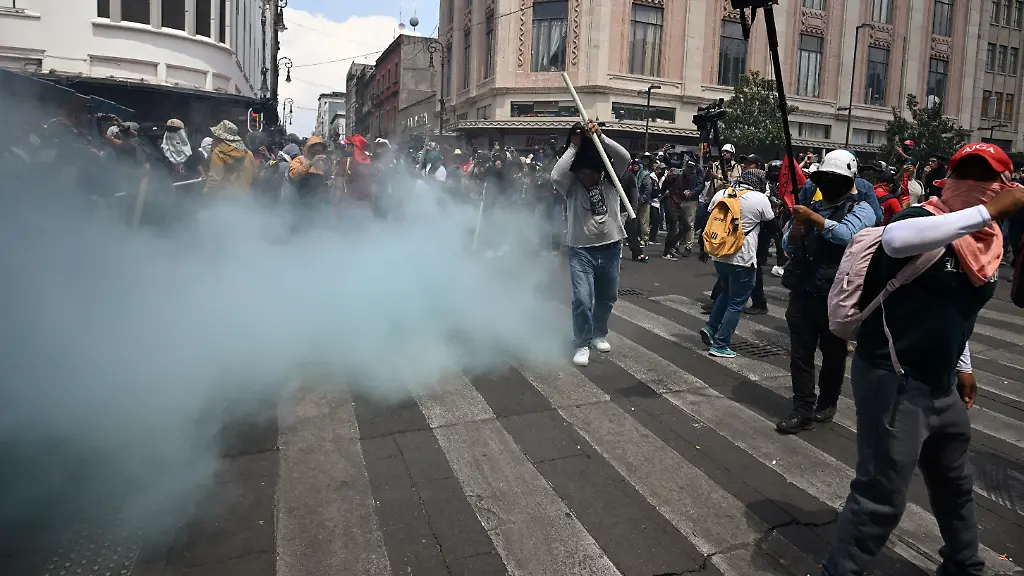 Teachers-stand-near-a-barricade-blocking-access-to-the-Zocalo-as-blue-smoke-from-a-fire-extinguisher-discharged-by-police-rises-from-the-other-side-during-a-demonstration-ahead-of-the-FIFA-World-Cup-2026-in-Mexico-City-on-June-1-2026