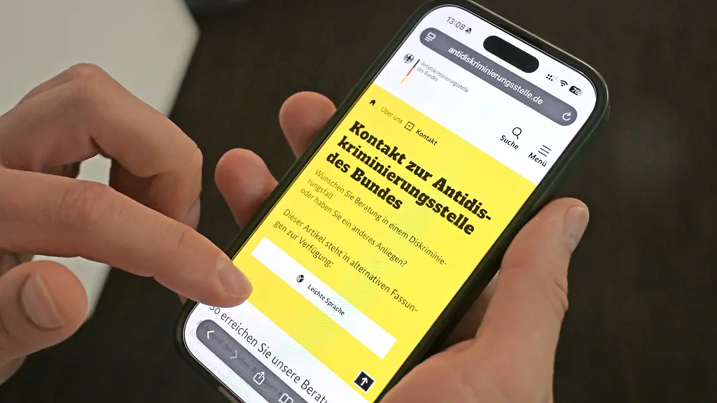 Ein-Mann-haelt-ein-Smartphone-in-der-Hand-und-ruft-die-Website-der-Antidiskriminierungsstelle-des-Bundes-auf-Auf-dem-Bildschirm-ist-das-Kontaktformular-der-Behoerde-zu-sehen-Die-Antidiskriminierungsstelle-des-Bundes-veroeffentlicht-am-02-06-2026-ihren-Jahresbericht-2025-der-einen-Ueberblick-ueber-die-Taetigkeit-der-Behoerde-und-aktuelle-Entwicklungen-gibt-Ein-Schwerpunkt-des-Berichts-liegt-auf-rassistischer-Diskriminierung