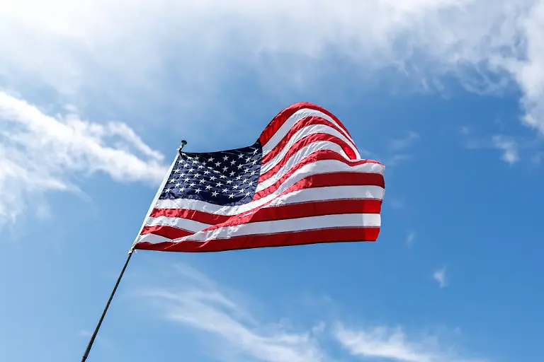 Die-Flagge-der-USA-United-States-of-America-Vereinigte-Staaten-von-Amerika-das-sogenannte-Sternenbanner-weht-an-einem-Fahnenmast-in-Grafenwoehr-Bayern-vor-dem-blauen-Himmel-im-Wind-Die-Stars-and-Stripes-besteht-aus-7-roten-und-6-weissen-Streifen-die-fuer-die-13-Gruendungsstaaten-stehen-und-aus-einem-blauen-Flaggenfeld-Goesch-im-linken-oberen-Eck-dessen-derzeit-50-weisse-Sterne-die-50-Bundesstaaten-der-amerikanischen-Staaten-symbolisieren