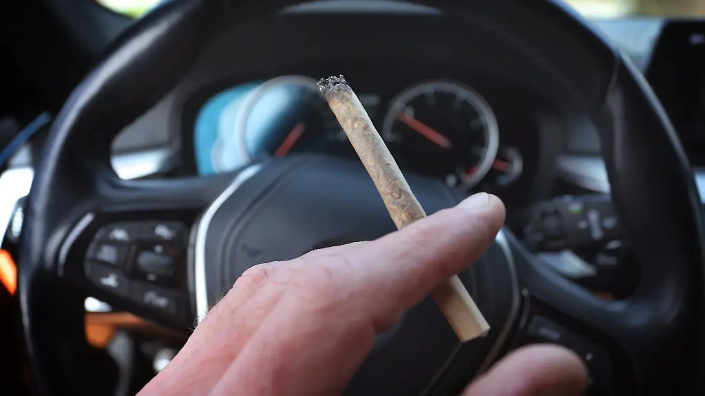 Ein-Mann-sitzt-mit-einem-Joint-zwischen-den-Fingern-am-Steuer-eines-Autos