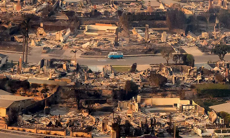 In-this-aerial-view-taken-from-a-helicopter-a-blue-van-sits-intact-amid-burned-homes-seen-from-above-during-the-Palisades-fire-near-the-Pacific-Palisades-neighborhood-of-Los-Angeles-California-on-January-9-2025-Massive-wildfires-that-engulfed-whole-neighborhoods-and-displaced-thousands-in-Los-Angeles-remained-totally-uncontained-January-9-2025-authorities-said-as-US-National-Guard-soldiers-readied-to-hit-the-streets-to-help-quell-disorder-Swaths-of-the-United-States-second-largest-city-lay-in-ruins-with-smoke-blanketing-the-sky-and-an-acrid-smell-pervading-almost-every-building