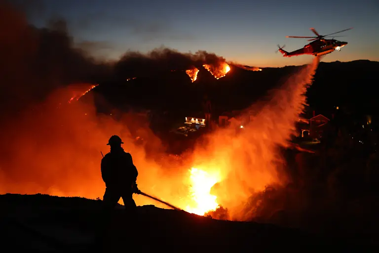 Fire-personnel-respond-to-homes-destroyed-while-a-helicopter-drops-water-as-the-Palisades-Fire-grows-in-Pacific-Palisades-California-on-January-7-2025-Terrified-residents-caught-in-blazing-neighbourhoods-influencers-ignoring-the-ban-on-drones-and-the-frightening-unpredictability-of-the-wildfires-are-just-some-of-what-journalists-covering-the-fires-ravaging-Los-Angeles-for-AFP-have-had-to-manage-The-United-States-second-largest-city-has-never-faced-a-blaze-of-this-scale-driven-by-an-extreme-autumn-drought-and-fierce-Santa-Ana-winds-the-strongest-since-2011-that-have-turned-dry-hills-into-kindling-fuelling-a-relentless-inferno-that-has-raged-for-more-than-a-week